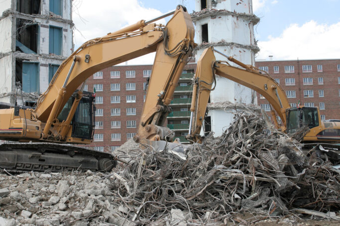 Two pieces of construction equipment demolishing a building